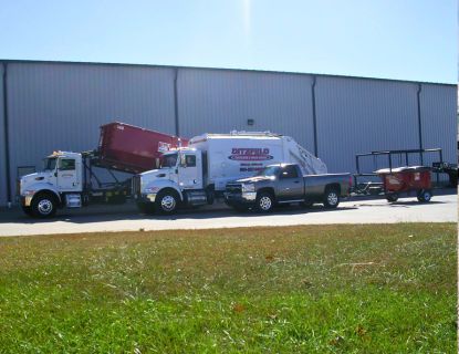 A variety or CDL-B tucks including a roll off container truck, a dump truck and a truck with a trailer hauling a dumpster.